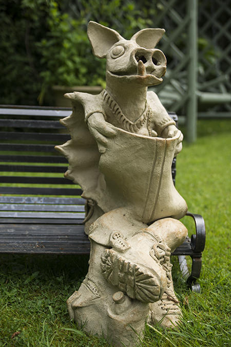 Playful dragon sculpture on a park bench reading a paper